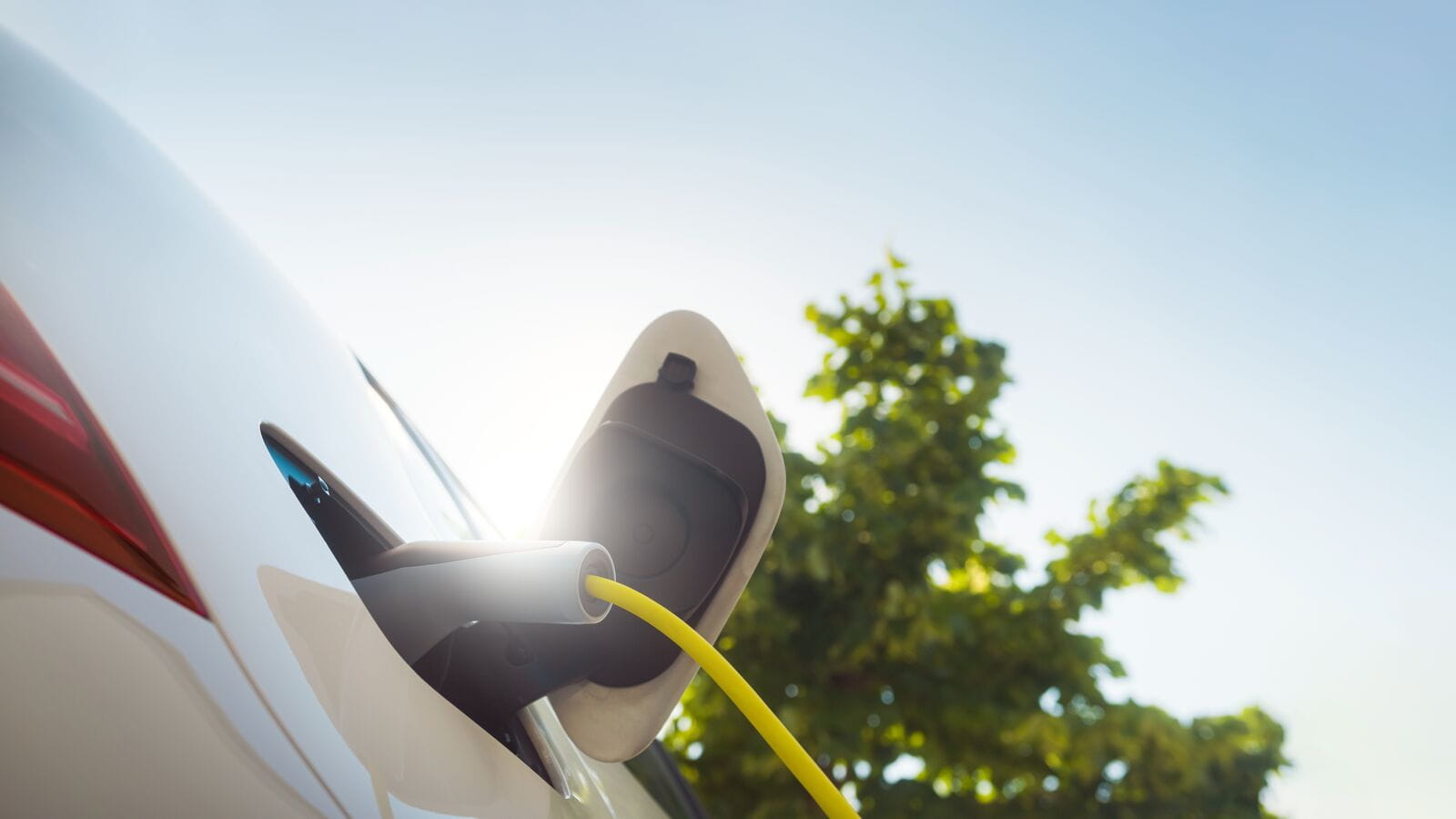 Close up shot of a white car being charged via a yellow cable