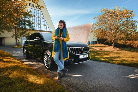 Kvinne som står foran en elbil og bruker mobiltelefonen.