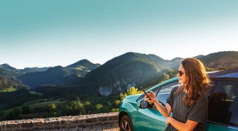 Mulher encostada ao carro com vista para a montanha