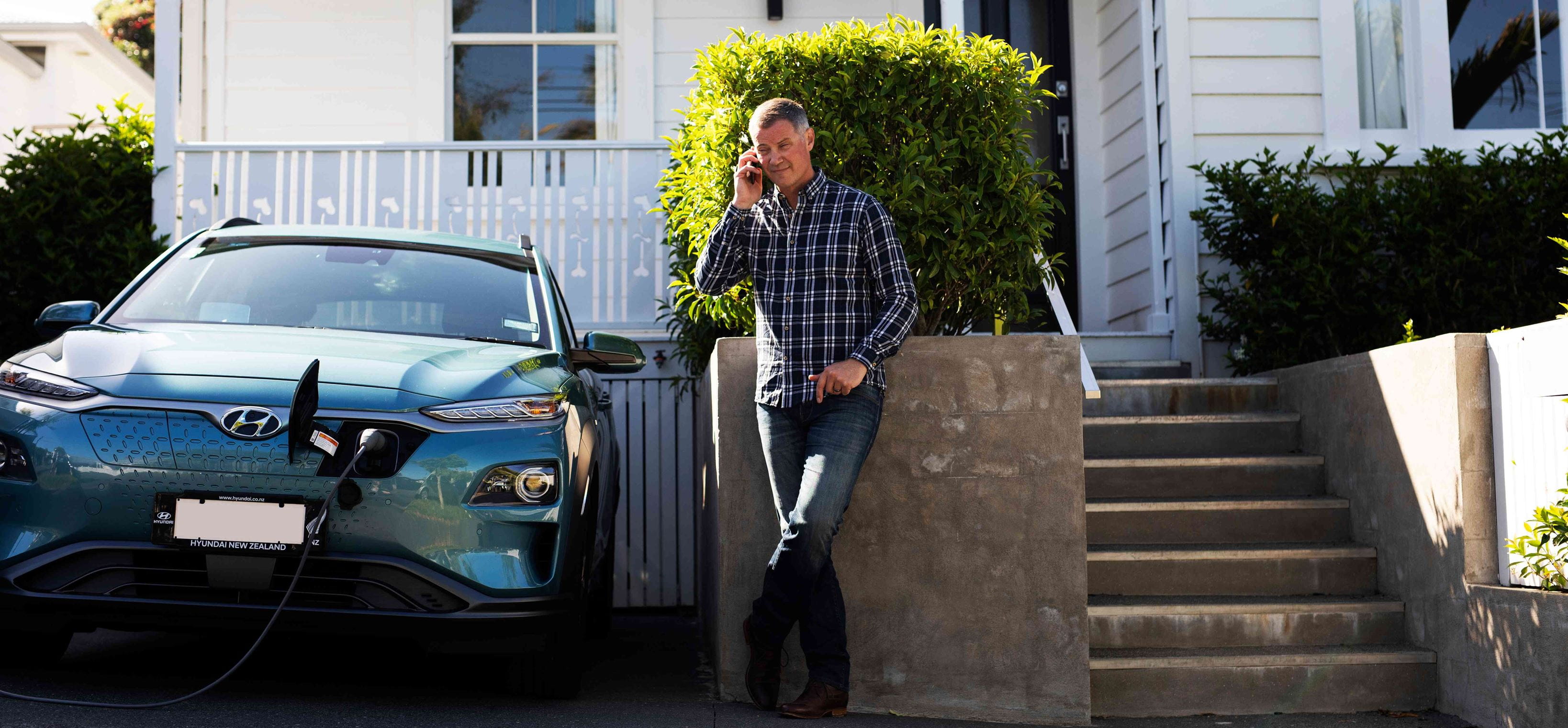A man talking on a cell phone in front of the house while the electric vehicle is charging