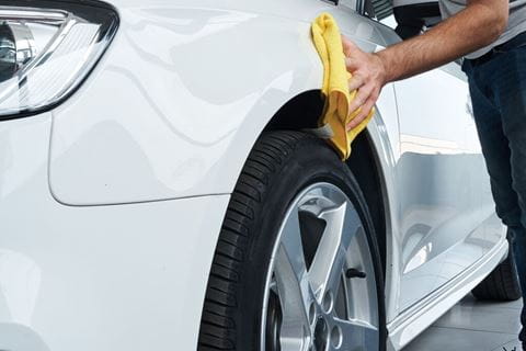 Close up view of a worker detailing polishing a white car with a rag after cleaning it